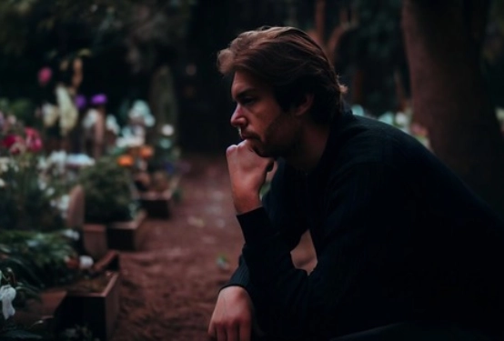 Hombre en un cementerio, sentado junto a flores, mostrando un momento de recuerdo y respeto.