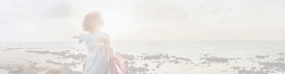 Mujer en la playa con los brazos abiertos, expresando alegría y conexión con la naturaleza.