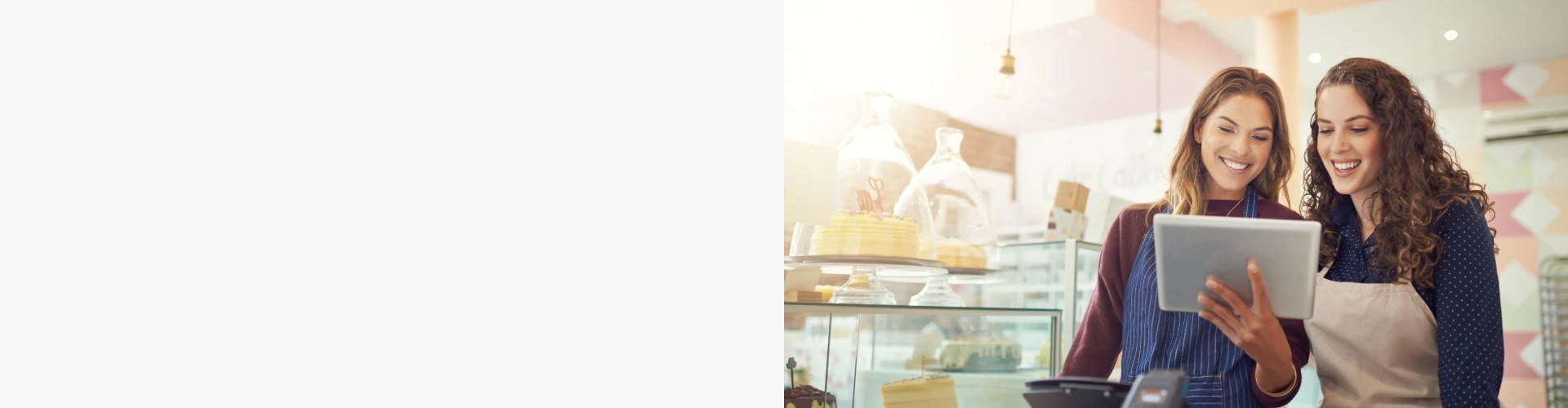 Dos personas revisando información en una tablet dentro de una pastelería, con vitrinas llenas de tartas y decoración moderna en el fondo.